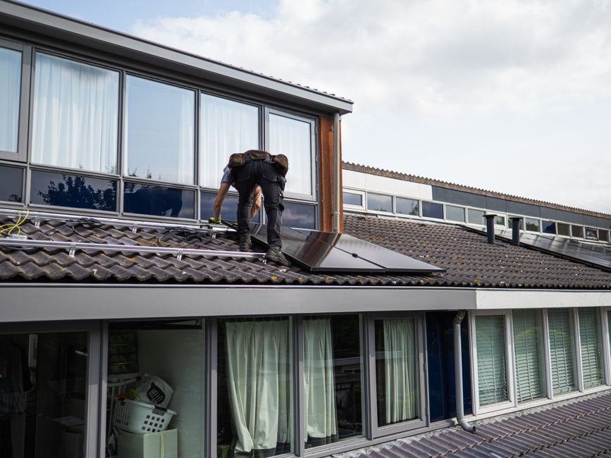 Installation d’un système d’alarme solaire autour d’une maison non raccordée en France, technicien positionnant les capteurs et le panneau solaire