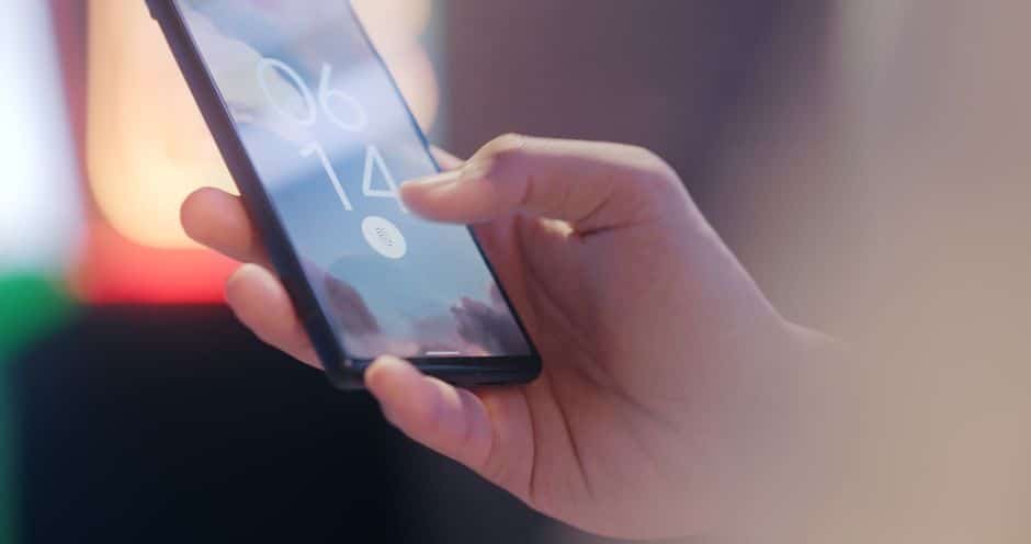 Gros plan sur une main tenant un smartphone affichant l’interface d’une application de vidéosurveillance maison, avec tableau de bord et flux vidéo en direct.