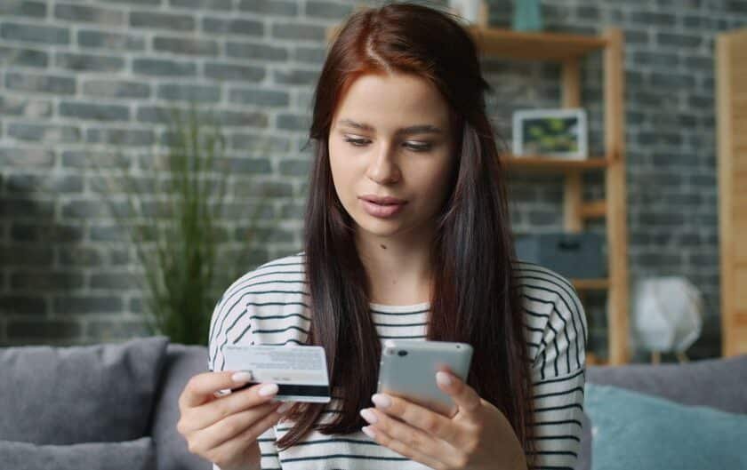 Femme française utilisant une application de vidéosurveillance maison sur son smartphone dans un salon moderne, pour piloter son alarme connectée.