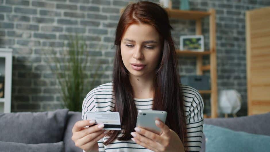Femme française utilisant une application de vidéosurveillance maison sur son smartphone dans un salon moderne, pour piloter son alarme connectée.