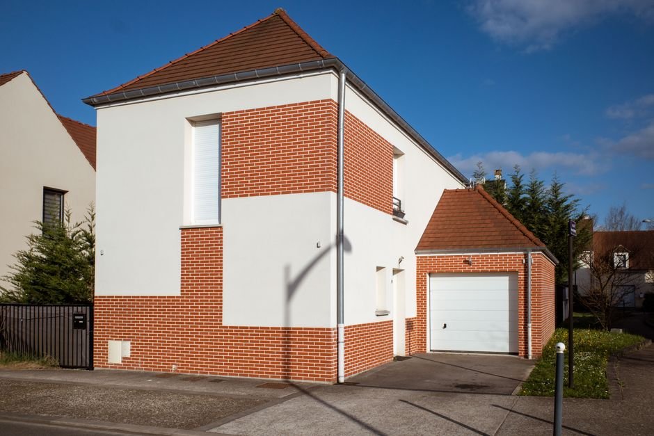 Maison individuelle moderne en France avec éclairages extérieurs allumés, volets fermés et panneau d’alarme visible, illustrant une habitation sécurisée avant les vacances