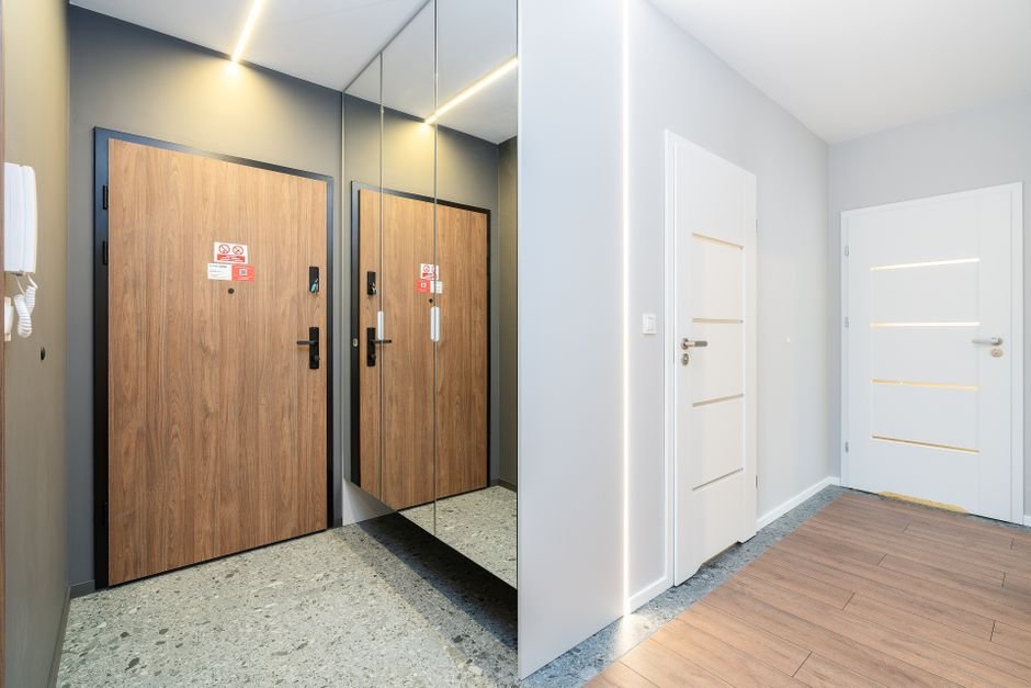 Vue du couloir d’un appartement en immeuble avec porte palière sécurisée, judas, interphone et accès au balcon, montrant les principaux points d’entrée à protéger